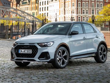 Een zilveren Audi A1 compacte crossover-SUV staat geparkeerd in een geplaveide straat met historische Europese gebouwen op de achtergrond en biedt alles wat je moet weten voor het verkennen van tijdloze charme en modern gemak.