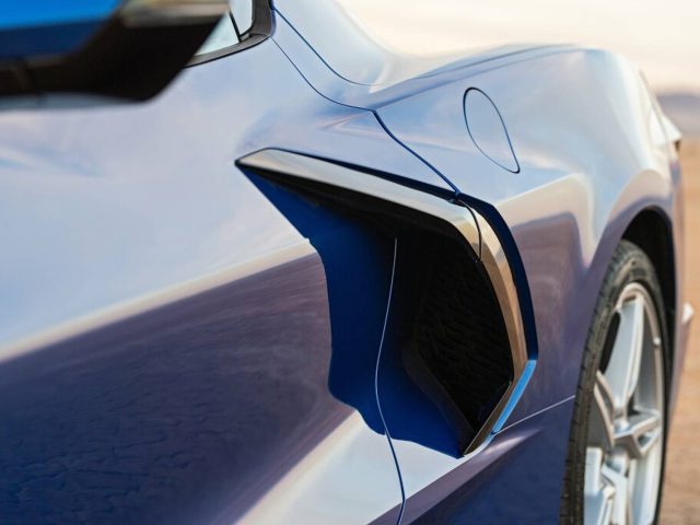 Close-up van de slanke zijventilatie en het achterwiel van een blauwe sportwagen van een Corvette op een wazige buitenachtergrond.