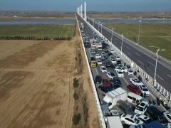 Luchtfoto van een snelweg met meerdere rijstroken met zwaar verkeer, inclusief auto's en vrachtwagens, die zich uitstrekt door een landelijk landschap met velden aan beide zijden. Temidden van de drukte blijkt er een kettingbotsing te zijn die voor flinke vertraging zorgt.