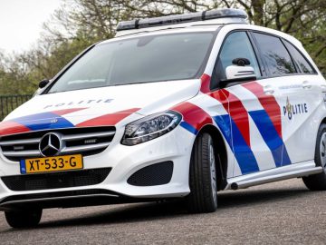 Buiten staat een witte Mercedes-Benz politieauto met Nederlandse opschriften en kenteken XT-533-G, met het opschrift "Politie", geparkeerd.