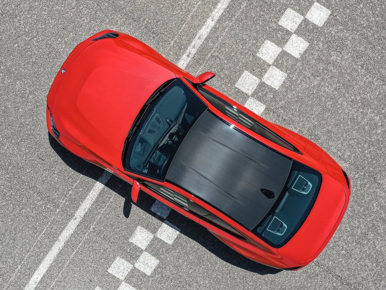 Bovenaanzicht van een rode sportwagen met zwarte motorkap, geparkeerd op een zebrapad op een asfaltweg. In de geest van ‘Vooruitblik Autojaar 2023’ is het duidelijk dat Gerbens visie op toekomstige auto’s al vorm krijgt.