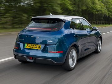 Een blauwe Ora Funky Cat hatchback rijdt over een weg met een onscherpe achtergrond, op het kenteken staat 'FJ22 DLK.