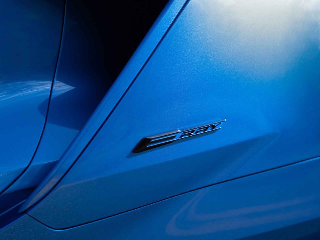 Close-up van de buitenkant van een blauwe Corvette E-Ray met een metalen badge met de tekst "ZR1".