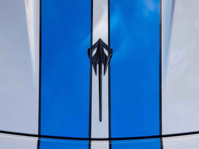 Close-up van een Corvette E-Ray-motorkap met een blauw ontwerp met dubbele strepen en een zwart, gestileerd embleem in het midden.