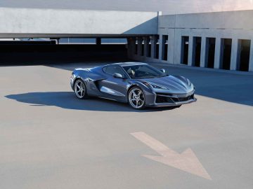 Een strakke, grijze Corvette E-Ray staat geparkeerd in een lege parkeergarage. De auto beschikt over moderne, aerodynamische ontwerpen en baadt in natuurlijk licht.