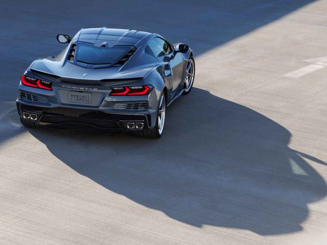 Een grijze Corvette E-Ray-sportwagen met zwarte details staat geparkeerd op een betonnen oppervlak en werpt een schaduw. Het strakke design en de achterlichten van de auto zijn duidelijk zichtbaar.