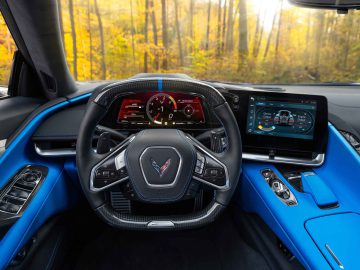 Het interieur van de Corvette E-Ray is voorzien van een gedetailleerd stuur met bedieningselementen, een digitaal instrumentenpaneel, een middenconsole met meerdere knoppen en een aanraakscherm met verschillende voertuiginstellingen.