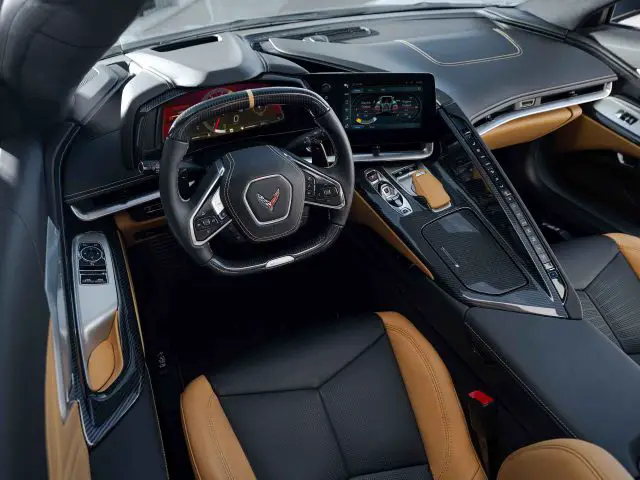 Het interieur van de Corvette E-Ray straalt de sfeer uit van een high-end sportwagen met een met leer bekleed stuurwiel met het iconische Corvette-logo, een digitaal dashboard, een touchscreen-infotainmentsysteem en luxe bruine en zwart lederen stoelen.