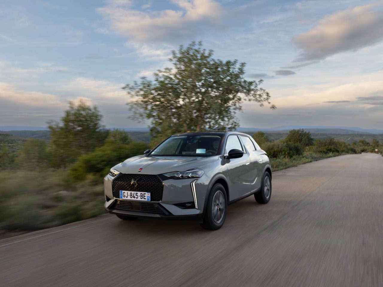 Een DS 3 SUV rijdt op een landelijke weg omgeven door groen en open lucht. Het kenteken van de auto is zichtbaar en toont een Europese registratie.