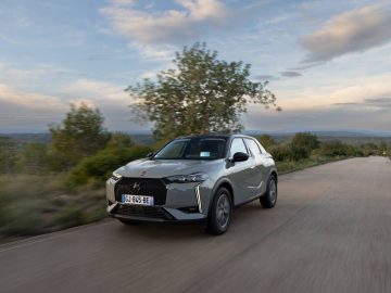 Een DS 3 SUV rijdt op een landelijke weg omgeven door groen en open lucht. Het kenteken van de auto is zichtbaar en toont een Europese registratie.