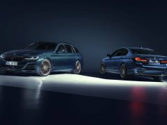 Twee donkergekleurde luxeauto's, een sedan en een stationwagen, tentoongesteld onder studioverlichting op een donkere achtergrond. Beide voertuigen hebben een sportief ontwerp en stijlvolle velgen, die het uitgesproken vakmanschap van Alpina belichamen.