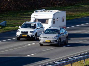Twee auto's en een vrachtwagen rijden op een snelweg met meerdere rijstroken; de ene auto trekt een tweedehands caravan, terwijl de andere auto en de vrachtwagen in aangrenzende rijstroken rijden.