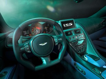 Binnenaanzicht van een luxe sportwagen met een stuur met het Aston Martin-logo, een digitaal dashboarddisplay en een middenconsole met een touchscreen met de tekst "DBS 770 Ultimate".