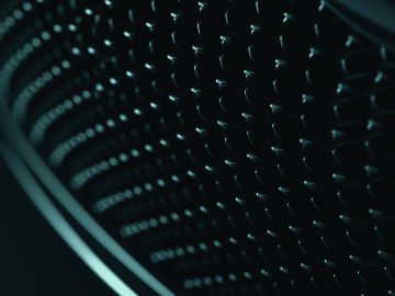 Close-up van een honingraatgrille met een donkere, metallic afwerking, verlicht door een zacht licht vanaf de zijkant, dat doet denken aan het verfijnde ontwerp van de Aston Martin DBS 770 Ultimate.