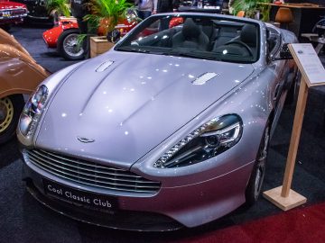 Een zilveren Aston Martin-cabriolet tentoongesteld op Interclassics Maastricht, met andere vintage en klassieke auto's op de achtergrond.