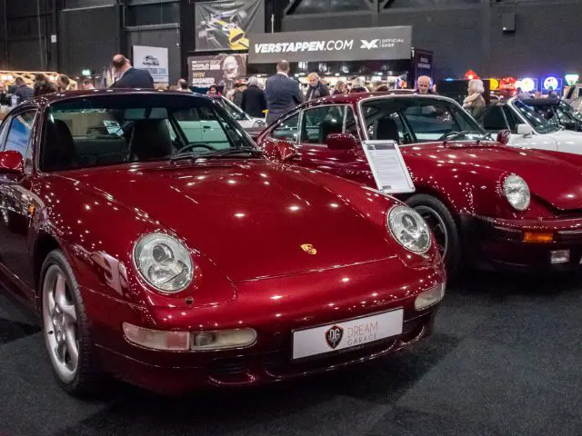 Twee rode Porsche sportwagens te zien op Interclassics Maastricht, met mensen op de achtergrond en diverse standhouders zichtbaar.