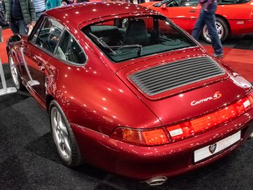 Een rode Porsche Carrera-auto, onderdeel van de tentoonstelling Interclassics Maastricht, wordt tentoongesteld op de vloer van een showroom, van achteren gezien met meerdere mensen op de achtergrond.