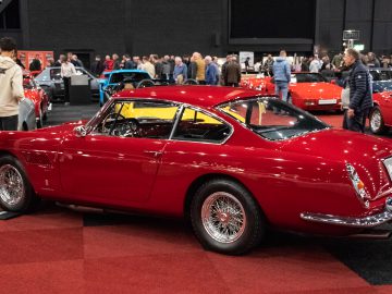 Een rode vintage auto die binnenshuis te zien is op de autoshow Interclassics Maastricht, met een menigte mensen op de achtergrond.