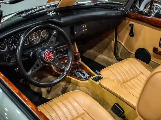 Binnenaanzicht van een vintage cabriolet bij Interclassics Maastricht, met een houten dashboard, een zwart stuur met embleem, bruin lederen stoelen en diverse bedieningselementen en meters.