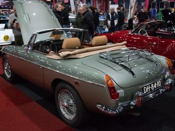 Een klassieke zilveren cabriolet met open kap te zien bij Interclassics Maastricht, omringd door mensen en andere oldtimers.