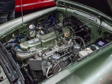 De motor van een klassieke auto met de motorkap open, met verschillende mechanische componenten en bedrading in een groene motorruimte, die doet denken aan wat je zou vinden bij Interclassics Maastricht.