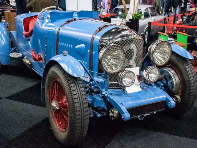 Een vintage blauwe raceauto met een grote grille en nummer 9 aan de voorkant, prominent tentoongesteld op Interclassics Maastricht naast andere prachtige voertuigen.