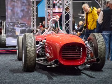 Bij Interclassics Maastricht is een rode vintage raceauto te zien, die de bewondering wekt van de aanwezigen op het auto-evenement.