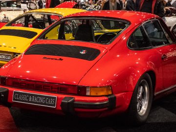 Op Interclassics Maastricht worden drie klassieke Porsche-auto's tentoongesteld, waaronder een rood, geel en wit model. Op de voorkant staat een bord met de tekst 'Classic & Racing Cars'.