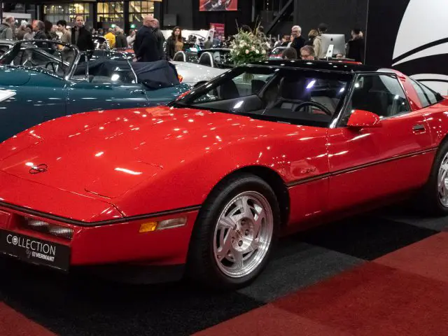 Een rode sportwagen die binnenshuis wordt tentoongesteld, met meerdere andere auto's op de achtergrond op de autoshow Interclassics Maastricht.