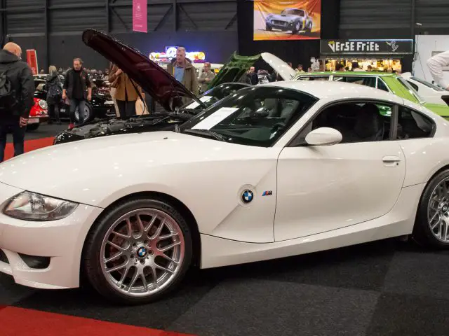 Een witte BMW Z4 coupé met open motorkap wordt tentoongesteld op Interclassics Maastricht en trekt verschillende mensen aan die zich rond het voertuig hebben verzameld.