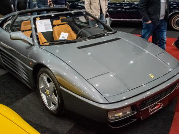 Op de indoor autotentoonstelling Interclassics Maastricht wordt een grijze sportwagen met cabriokap tentoongesteld, met informatiebladen op de bestuurdersstoel en middenconsole.