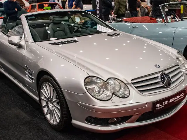 Een zilveren Mercedes-Benz SL55 AMG cabriolet tentoongesteld op Interclassics Maastricht. De auto heeft twee deuren, een strak zwart interieur en staat tussen andere vintage voertuigen, waardoor hij de toeschouwers fascineert met zijn tijdloze elegantie.