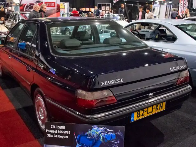 Afbeelding van een donkerblauwe Peugeot 605 SV24 te zien bij Interclassics Maastricht. Op het kenteken staat "82-LJ-KN." Op de achtergrond zijn andere auto's en mensen zichtbaar.