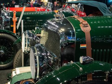 Een close-up van vintage groene auto's tentoongesteld op Interclassics Maastricht. De auto's zijn voorzien van chromen details en leren riemen, met mensen op de achtergrond.