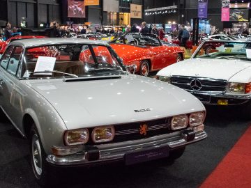 Naast een witte klassieke cabriolet staat op Interclassics Maastricht een zilveren klassieker met Peugeot-embleem, omringd door diverse andere oldtimers.