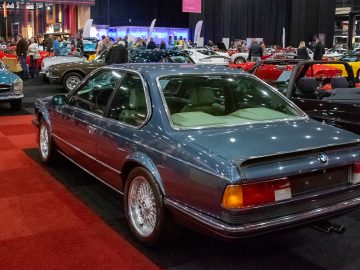 Een blauwe klassieke BMW-auto wordt binnen tentoongesteld op de show Interclassics Maastricht, omringd door andere vintage voertuigen en mensen.