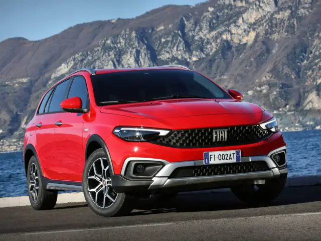 Een rode Fiat Tipo Cross-auto geparkeerd nabij water en bergen.