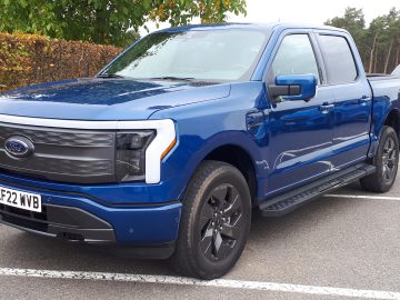 Op een parkeerplaats staat een blauwe Ford-pick-up geparkeerd, met kenteken EF22 KVB. Op de achtergrond zijn bomen en een ander voertuig zichtbaar, wat een serene vooruitblik autojaar 2023 biedt.