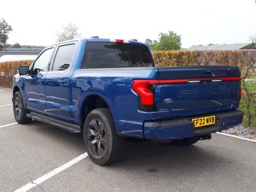 Een blauwe Ford F-150 Lightning geparkeerd op een parkeerplaats, gezien vanaf de bestuurderszijde achterin. Met het kenteken "FF22 VVB" vertegenwoordigt dit voertuig perfect vooruitblik autojaar 2023.