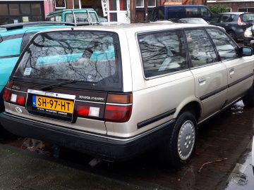 Een beige Toyota Camry stationwagen staat geparkeerd in een straat tussen een blauwe auto en een witte auto en valt op door zijn klassieke design.