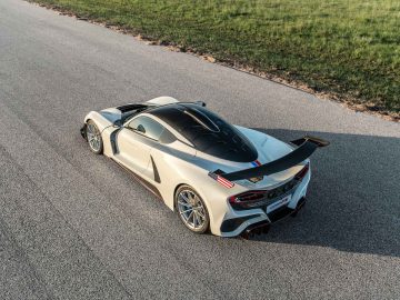 Bovenaanzicht van een Hennessey Venom F5 Revolution Coupé, waarvan het hoogwaardige sportwagenontwerp er strak uitziet terwijl hij geparkeerd staat op een verharde weg naast een grasveld.