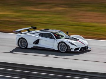 Een Hennessey Venom F5 Revolution Coupé, met zwarte accenten en een achterspoiler, snelt op een racecircuit en laat de achtergrond wazig.