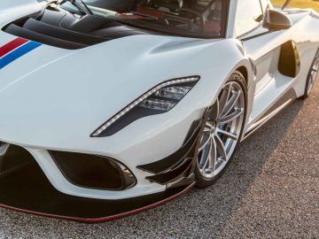 Close-up van een slanke, witte Hennessey Venom F5 Revolution Coupé met aerodynamisch ontwerp, prominente luchtinlaten vooraan en zilverkleurige lichtmetalen velgen, geparkeerd op een asfaltoppervlak.