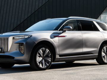 Een strakke, zilverkleurige SUV met een modern design, verticaal uitgelijnde grille en stijlvolle koplampen biedt een vooruitblik op autojaar 2023 terwijl hij buiten geparkeerd staat.