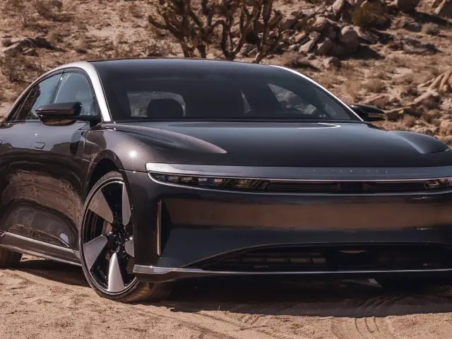 Een strakke zwarte elektrische auto geparkeerd op een zanderig, woestijnachtig terrein met rotsformaties en schaarse woestijnvegetatie op de achtergrond zorgt voor een verbluffende vooruitblik op autojaar 2023.