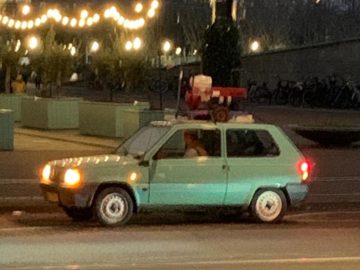 Een lichtgroene elektrische Fiat Panda hatchback staat 's nachts langs de kant van de weg geparkeerd met verschillende spullen op het dak vastgebonden.