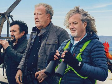 Drie mannen staan buiten, elk met een verrekijker in de hand. Ze zijn gekleed voor koud weer met jassen en handschoenen. Naast hen staat een haan, die doet denken aan een scène waarin Jeremy Clarkson zich zou kunnen bevinden. Op de achtergrond zijn een auto en een landelijk landschap zichtbaar.