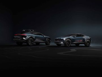Twee gestroomlijnde, futuristische elektrische SUV-conceptauto's met aerodynamische ontwerpen worden getoond op een donkere achtergrond en laten de moderne autotechnologie zien. Het ene voertuig heeft een imperiaal, het andere niet. Deze modellen belichamen innovatie, die doet denken aan de Audi Activesphere Concept.