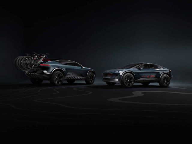 Twee donkergekleurde Audi Activesphere Concept SUV-auto's worden tentoongesteld in een slecht verlichte omgeving. Eén voertuig heeft een fietsenrek met fietsen achterop. Beide auto's hebben een strak ontwerp en grote banden, die een futuristische visie op avontuur en innovatie belichamen.