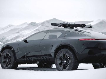 Een strakke, zwarte Audi Activesphere Concept SUV staat geparkeerd in een besneeuwd landschap met bergtoppen op de achtergrond. Het voertuig heeft een snowboard op het dak gemonteerd.